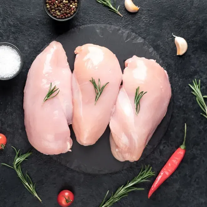 Raw chicken breasts on a dark cutting board with rosemary